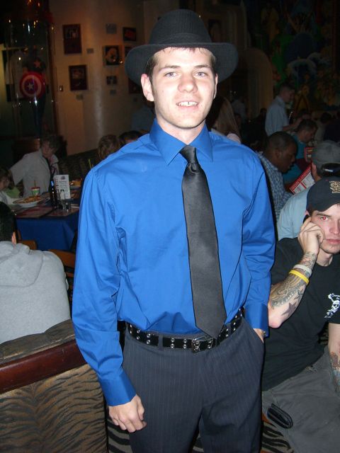 1996 Ford Probe - A man wearing a blue dress shirt, black tie, and fedora poses for a photo in a busy indoor venue.