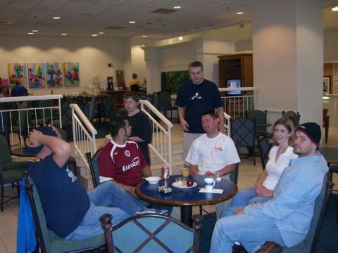 1996 Ford Probe - Several people are gathered in a hotel lobby, some seated at a table with drinks and snacks, others standing nearby.