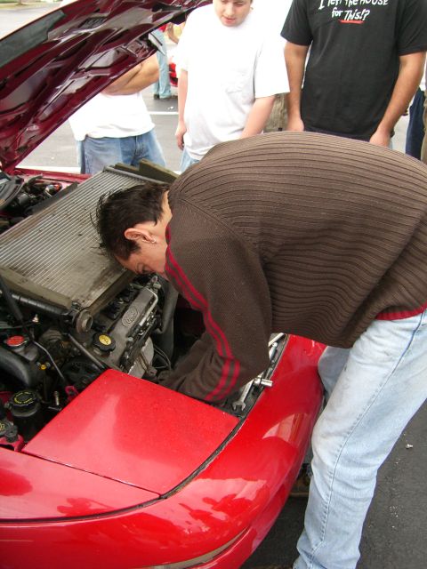 1996 Ford Probe - A group of people gather around the open hood of a red car, with one person leaning in to examine the engine.