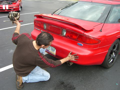 1996 Ford Probe - Man inspects the rear bumper of a red 1996 Ford Probe while another car sits nearby.