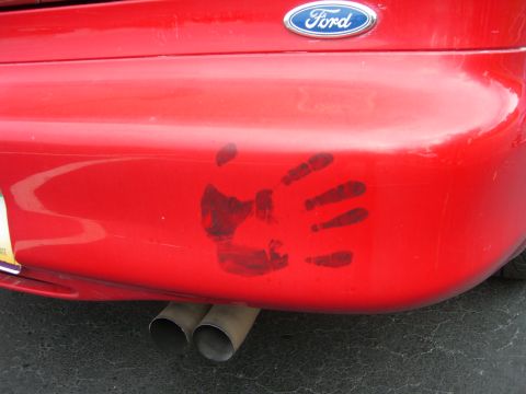 1996 Ford Probe - A handprint is visible on the rear bumper of a red car, above its dual exhaust pipes.