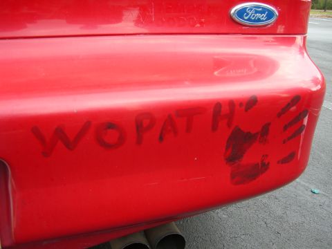 1996 Ford Probe - The rear bumper of a red car displays the words "WOPATH" and a handprint.