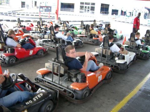 1996 Ford Probe - Several go-karts are parked in a line at an outdoor track, with people seated in some of them.