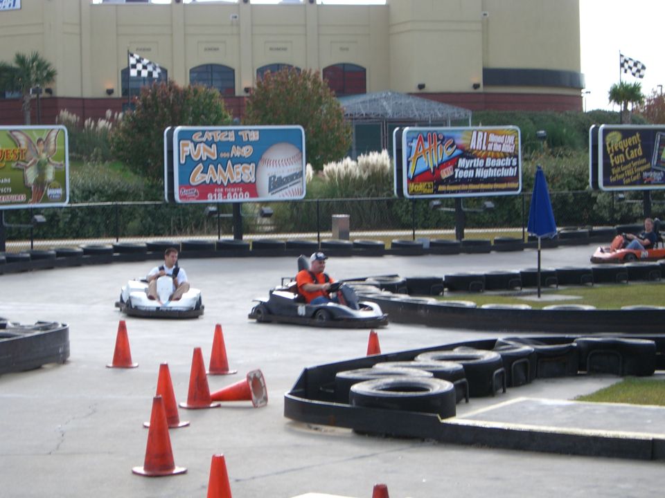 Go-karts on a track with orange cones and billboards in the background
