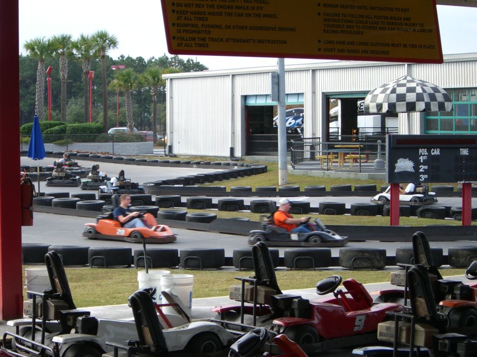 Go-karts racing on a track with palm trees and a building in the background