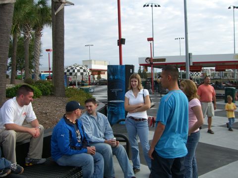 1996 Ford Probe - People socialize in an outdoor area with a checkered umbrella and gas station in the background.