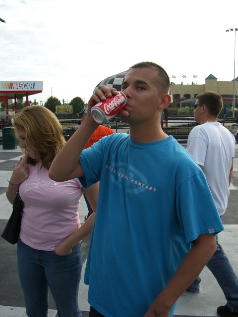 1996 Ford Probe - A man drinks a Coca-Cola while standing at a NASCAR track with other people in the background.