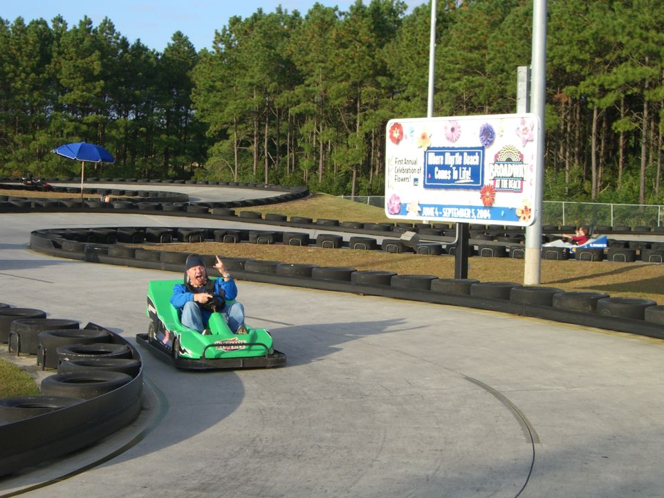 Go-kart track with a person in a green go-kart. Sign in background reads 'Broadway at the Beach'