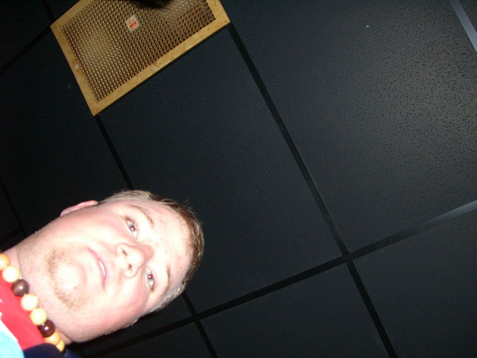 Man wearing a beaded necklace looks up towards a ceiling vent