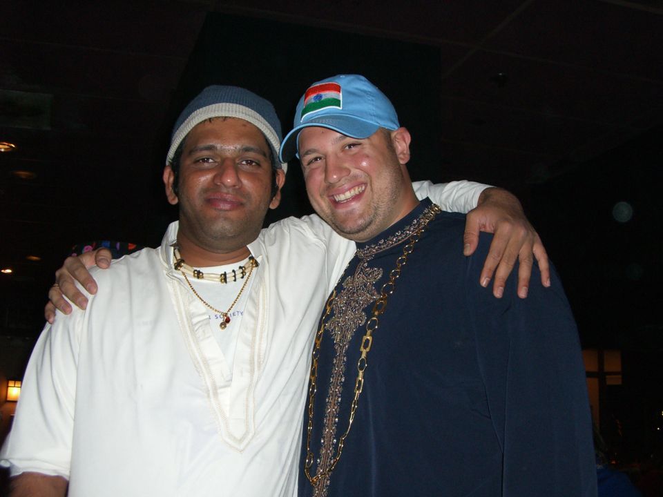 Two men, one wearing a blue cap with an Indian flag, the other a white cap, pose with arms around each other