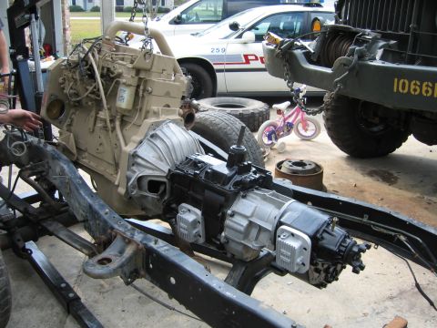 1986 Chevrolet Blazer - An engine and transmission assembly is suspended by a hoist, with other vehicles and a child's bicycle nearby.