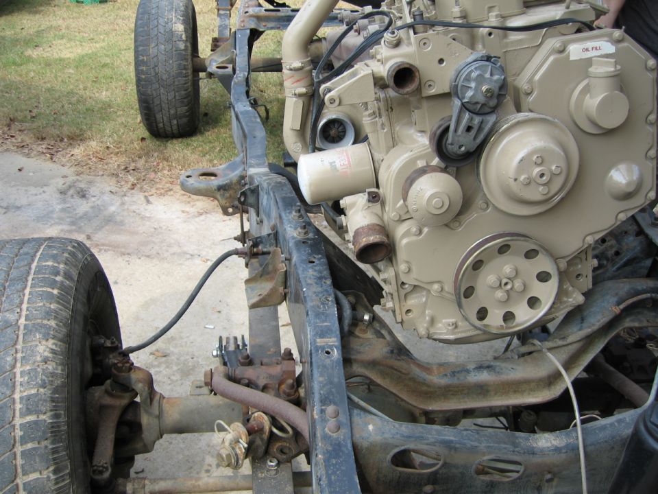 Tan diesel engine mounted in a bare stripped truck frame during a chassis build