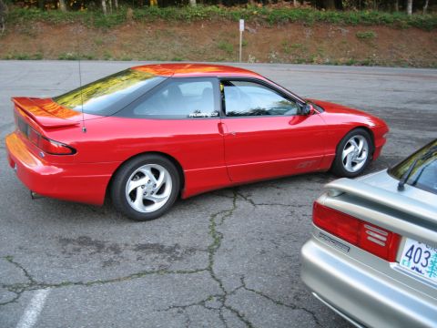 1996 Ford Probe - A red coupe is parked on cracked asphalt, with another vehicle partially visible in the foreground.