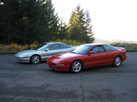 1996 Ford Probe - Two Ford Probe coupes are parked side-by-side in an outdoor lot with trees and foliage behind them.