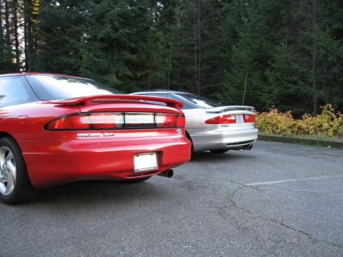 1996 Ford Probe - Two Ford Probes, one red and one silver, are parked in a lot with trees in the background.