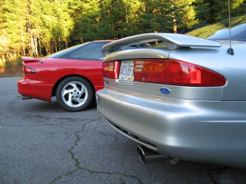 1996 Ford Probe - Two Ford Probes are parked side-by-side in front of a wooded area. The silver car's license plate is visible.