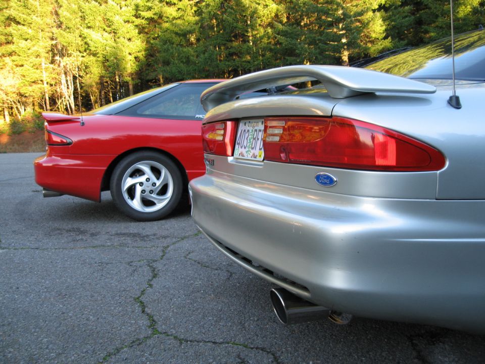 Two Ford Probes parked, one silver and one red. The silver one is in the foreground, showing its rear bumper and taillight