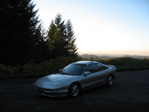 1996 Ford Probe - A silver coupe is parked outdoors during the golden hour, with a scenic view of rolling hills and trees.