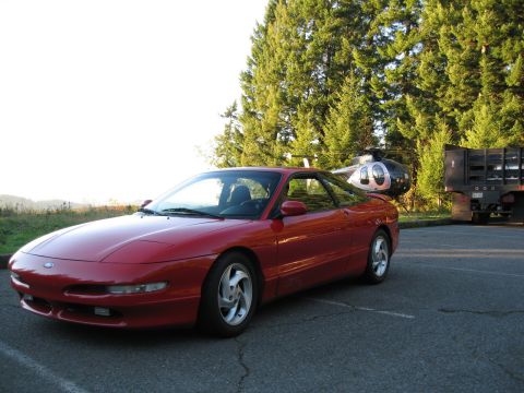 1996 Ford Probe - Red 1996 Ford Probe parked in a lot with a helicopter and truck in the background.