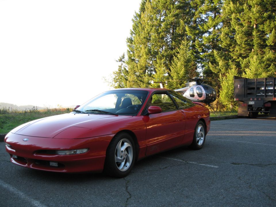 1996 Ford Probe parked next to a helicopter and a flatbed truck