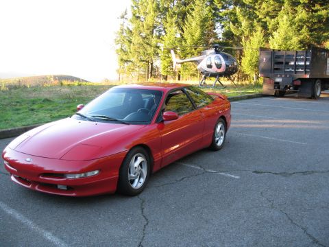 1996 Ford Probe - A red 1996 Ford Probe is parked in a lot, with a helicopter and a flatbed truck in the background.