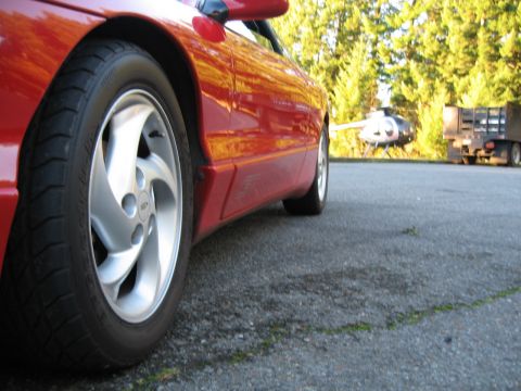 1996 Ford Probe - A red car is parked next to a helicopter and a truck, with trees in the background.