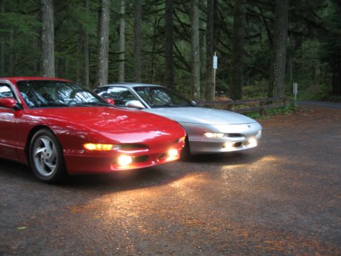 1996 Ford Probe - Two Ford Probes are parked side-by-side in a wooded area, with their headlights on.