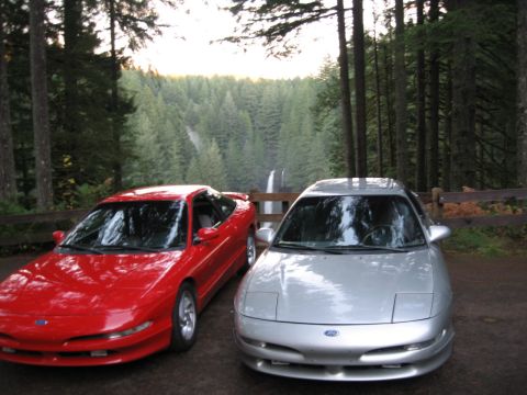 1996 Ford Probe - Two Ford Probes are parked in a scenic forest location with a waterfall in the background.