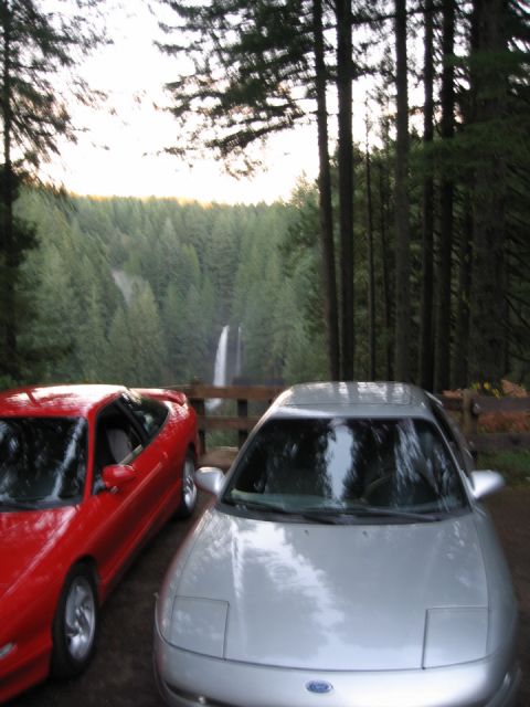 1996 Ford Probe - Two Ford Probes are parked in front of a scenic waterfall and dense forest.