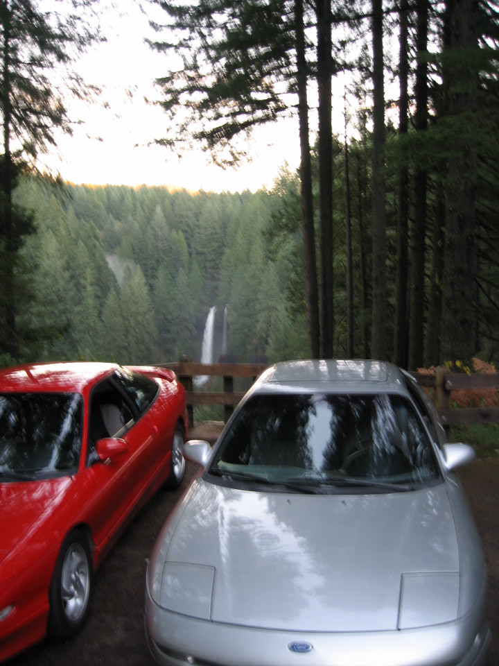 Silver Ford Probe and red Ford Probe parked with waterfall backdrop