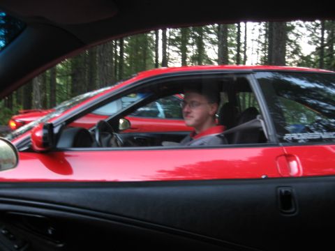 1996 Ford Probe - A man drives a red coupe, with another red car visible behind it, on a tree-lined road.