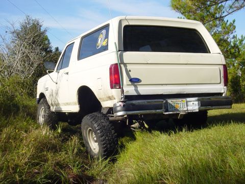 1989 Ford Bronco - This lifted white Ford Bronco is viewed from the rear in a grassy outdoor setting.