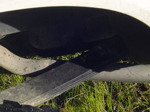 1989 Ford Bronco - Close-up view of the rear leaf spring suspension system on a vehicle, with grass visible below.