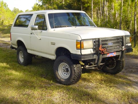 1989 Ford Bronco - A white 1989 Ford Bronco is shown from a 3/4 front view, off-road tires and a custom bumper.