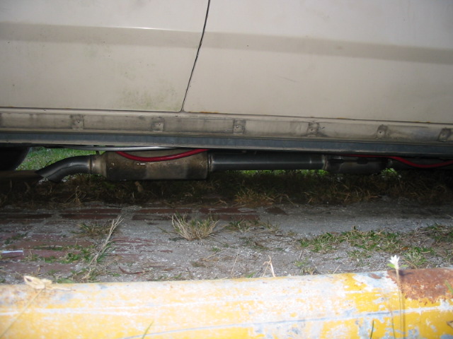 Underside view of a vehicle's exhaust pipe and muffler, with red wiring visible