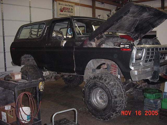 Black 1978 Ford Bronco with lifted suspension and large tires, hood open, parked in a garage