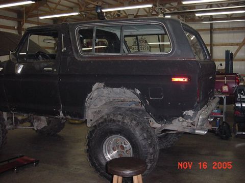 1978 Ford Bronco - This black Ford Bronco is parked inside a garage, showing off its large off-road tires and some bodywork in progress.