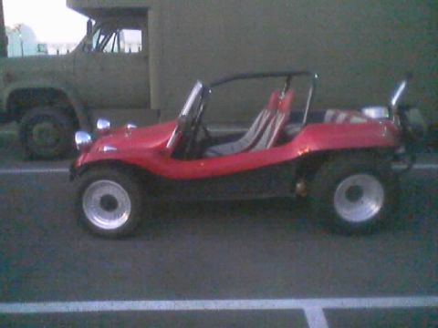 1990 Ford Bronco - red fiberglass dune buggy with chrome wheels sits in a parking lot next to a green flatbed military-style truck.