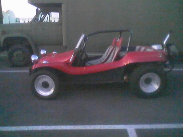 Red fiberglass dune buggy parked beside a green military truck
