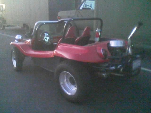 Red dune buggy with roll cage and chrome wheel parked in a garage area