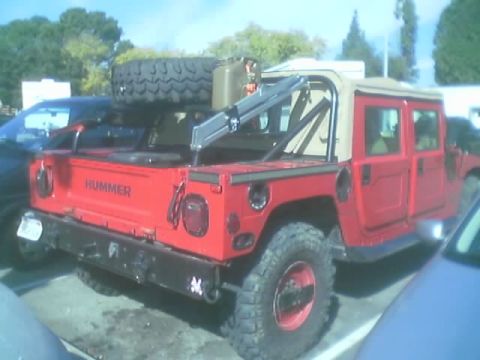 1990 Ford Bronco - red Hummer H1 with a tan soft top, roof-mounted spare tire and HUMMER lettering on the tailgate, parked outdoors.