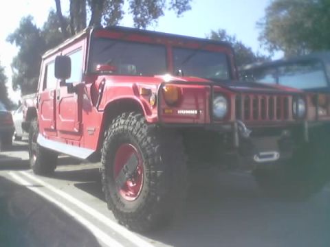 1990 Ford Bronco - red Hummer-badged vehicle with large off-road tires and red wheels parked in a sunny lot, front three-quarter view.