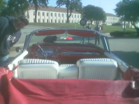 1968 Ford Mustang - Interior view of a red convertible with white seats, showing the dashboard and a person observing the vehicle.