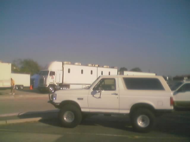 White Ford Bronco side view with large tires. Semi-truck in background