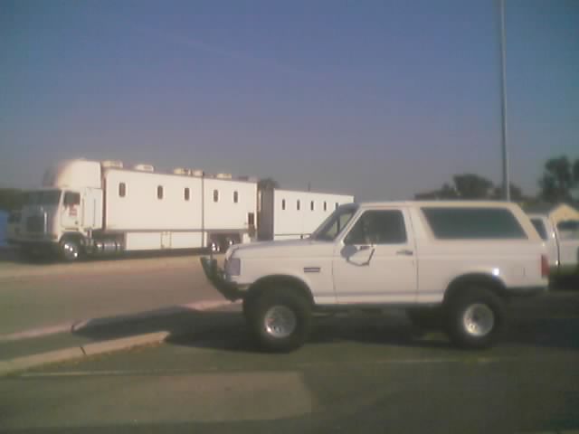 White lifted Ford Bronco SUV parked beside a semi truck and trailer
