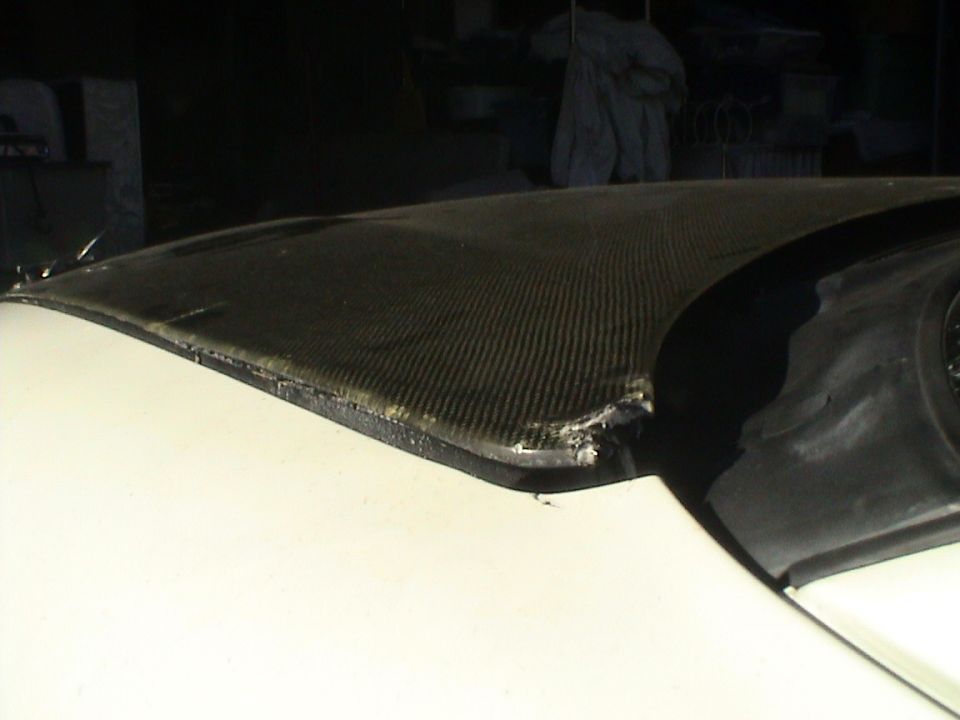 Damaged edge of a carbon fiber car hood, showing frayed material and impact marks