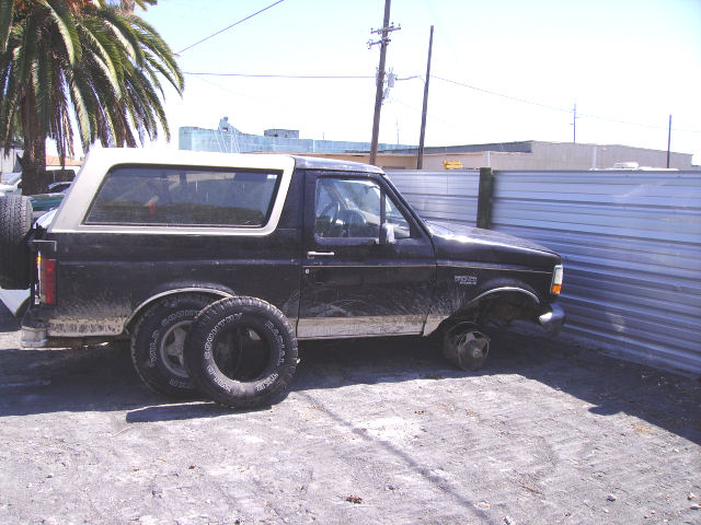 Black Ford Bronco with a white top, missing front passenger wheel, spare tire on rear