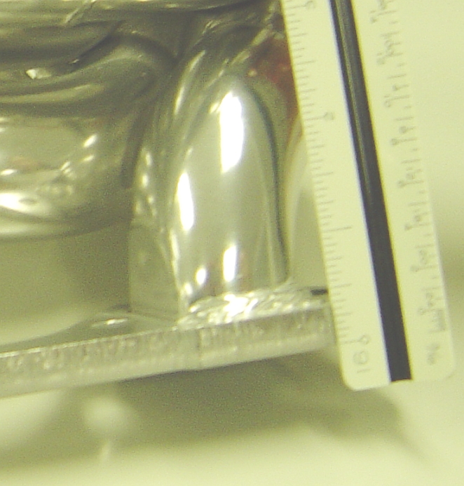 Close-up of a shiny metal exhaust manifold with a ruler for scale. Text at bottom says SUPERMOTORS.NET
