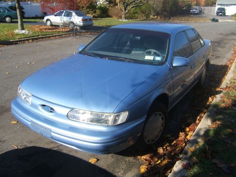 1994 Ford Taurus - A blue 1994 Ford Taurus sedan is parked on a residential street with fallen leaves on the ground.