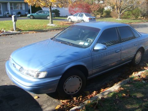 1994 Ford Taurus - Blue 1994 Ford Taurus parked on a street with fall foliage visible.